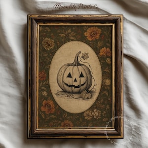 May include: A framed print featuring a central oval illustration of a carved jack-o'-lantern pumpkin with a vine, set against a dark green background with orange and brown floral patterns. The frame is dark wood with gold trim. Text reads Moonlite Prints Co.