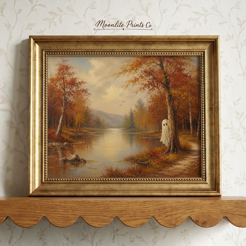May include: A framed landscape painting in a gold frame featuring an autumn forest scene with a lake and a small white ghost figure standing by a tree. The text Moonlite Prints Co is printed at the top center of the artwork in a dark script font.