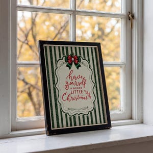 May include: A framed rectangular print featuring a cream-colored center with the red text "have yourself A MERRY LITTLE Christmas" and a green bow graphic. The background has vertical dark green stripes, all enclosed in a distressed black frame.