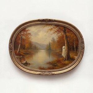 May include: An oval-framed oil painting depicting an autumn landscape with a calm lake, golden-hued trees, and a small white ghost figure standing beside a tree trunk on the right bank. The frame is ornate, metallic gold, and features decorative carvings.