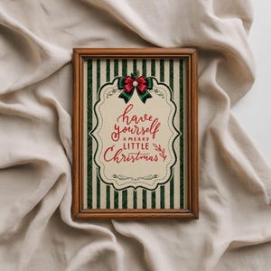 May include: A rectangular wooden frame containing a print with a dark green and cream vertical striped background. The center features a cream-colored scalloped label with the red text "have yourself A MERRY LITTLE Christmas" and a red and green bow.