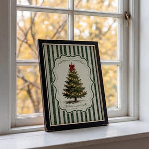 May include: A framed print featuring a green and white vertical striped background with a central decorative scalloped frame. Inside the frame is an illustration of a Christmas tree topped with a red bow and adorned with small glowing lights.