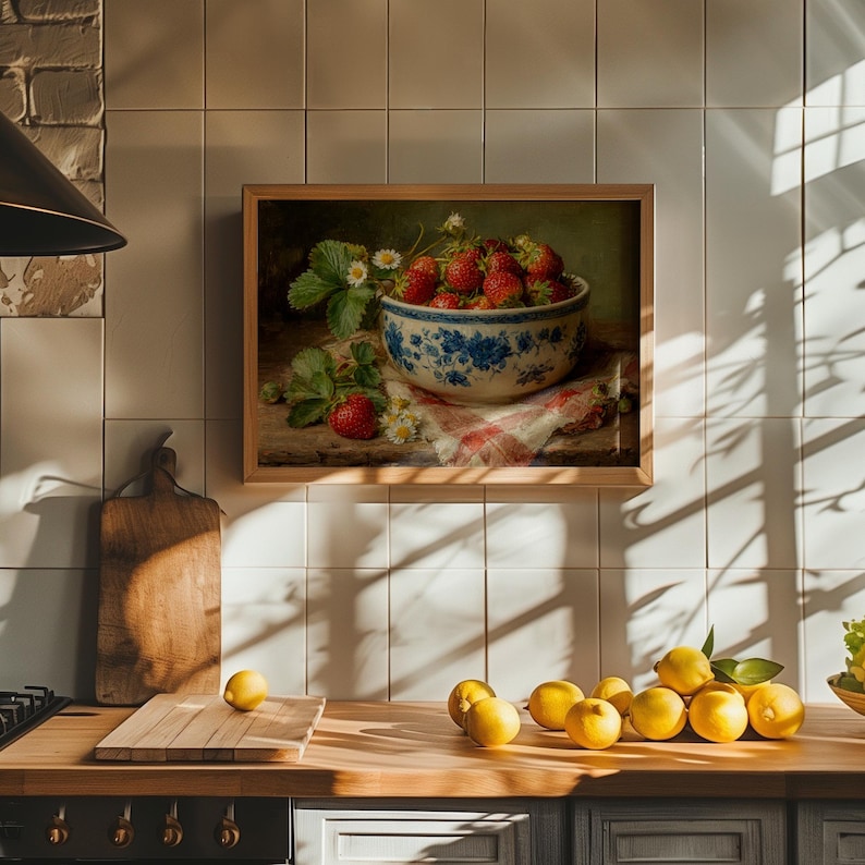 May include: A framed wall art print depicting a ceramic bowl filled with fresh red strawberries and green leaves, resting on a checkered cloth. The bowl features a blue floral pattern, and small white flowers are scattered near the fruit.