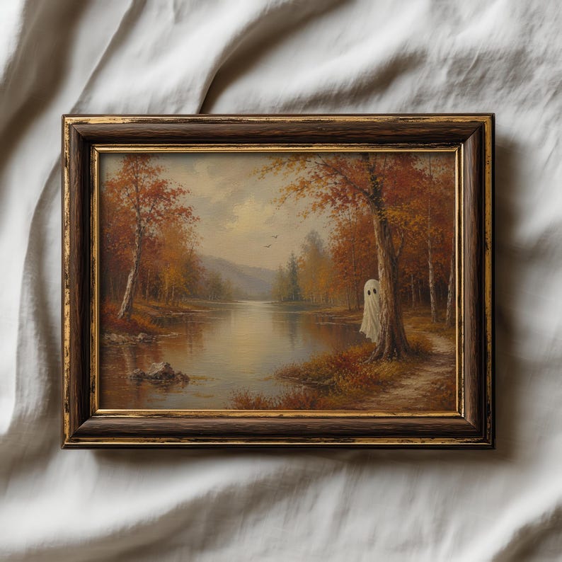 May include: A framed landscape painting featuring a calm lake surrounded by autumn trees with orange and brown foliage. A white ghost figure stands partially hidden behind a large tree trunk on the right side of the path near the water's edge.
