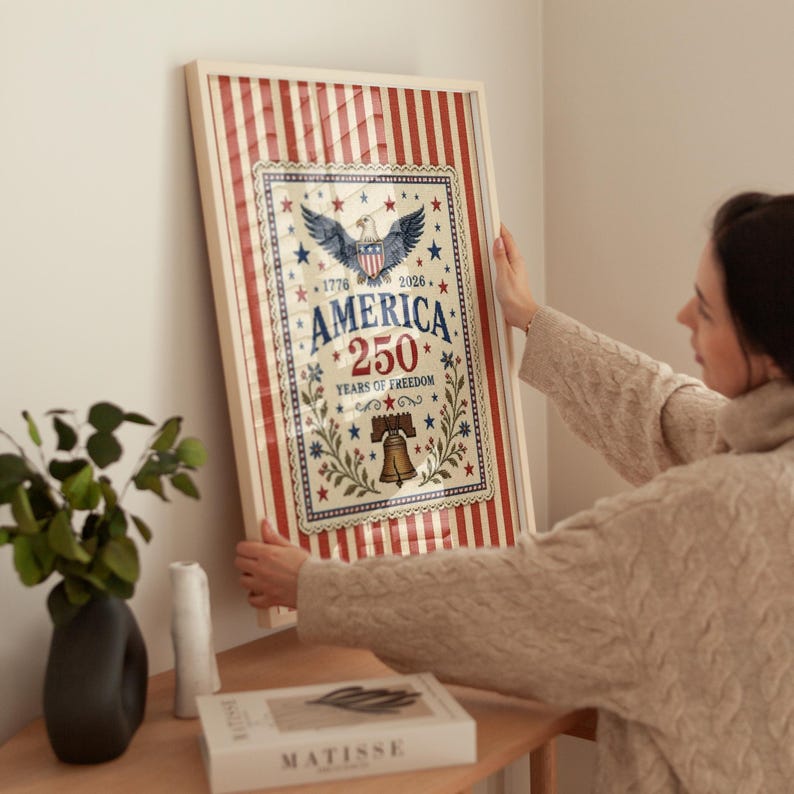 Puede incluir: Obra de arte enmarcada que celebra el 250 aniversario de Am&eacute;rica. El dise&ntilde;o presenta un &aacute;guila, estrellas y una campana, con el texto "AMERICA 250 YEARS OF FREEDOM". El marco tiene rayas rojas y blancas.