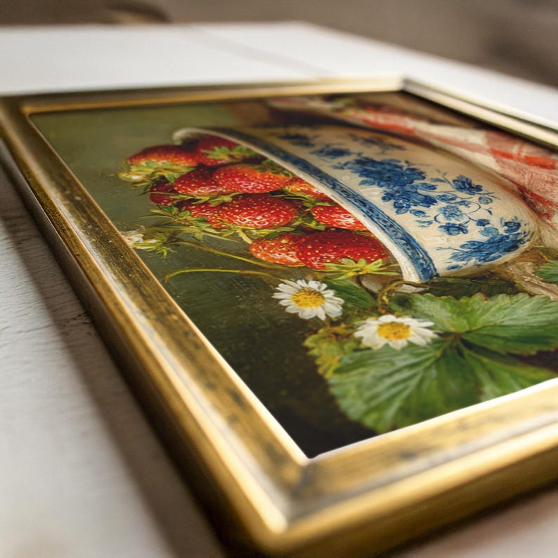 May include: A framed oil painting depicting a white ceramic bowl with blue floral patterns filled with bright red strawberries. The composition includes green strawberry leaves and small white daisy flowers, all enclosed within a metallic gold frame.