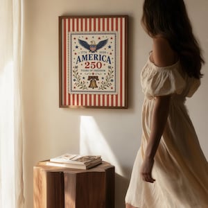 Puede incluir: Un estampado enmarcado con tem&aacute;tica patri&oacute;tica. El estampado presenta un fondo a rayas rojas y blancas con un dise&ntilde;o central que incluye un &aacute;guila, estrellas y el texto "AMERICA 250 YEARS OF FREEDOM". El marco es de color marr&oacute;n oscuro.