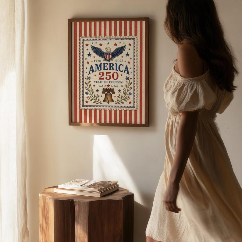 Puede incluir: Un estampado enmarcado con tem&aacute;tica patri&oacute;tica. El estampado presenta un fondo a rayas rojas y blancas con un dise&ntilde;o central que incluye un &aacute;guila, estrellas y el texto "AMERICA 250 YEARS OF FREEDOM". El marco es de color marr&oacute;n oscuro.