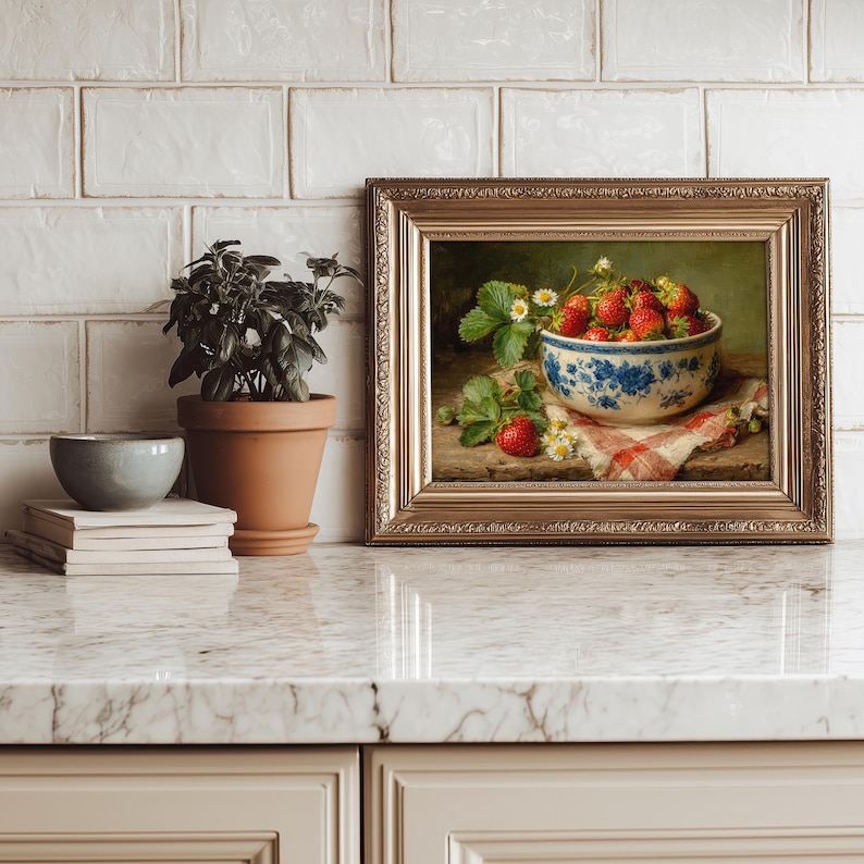 May include: A framed oil painting depicting a bowl of red strawberries with green leaves and small white flowers. The bowl features a blue floral pattern and sits on a red and white checkered cloth. The frame is ornate, metallic gold, and rectangular.