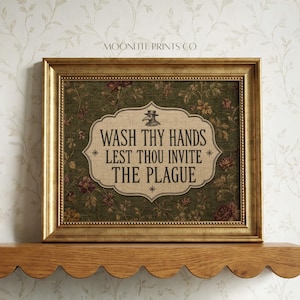 May include: A framed wall art print featuring a dark green background with a floral pattern and a central beige label. The text reads: WASH THY HANDS LEST THOU INVITE THE PLAGUE, accompanied by a small illustration of a plague doctor mask.