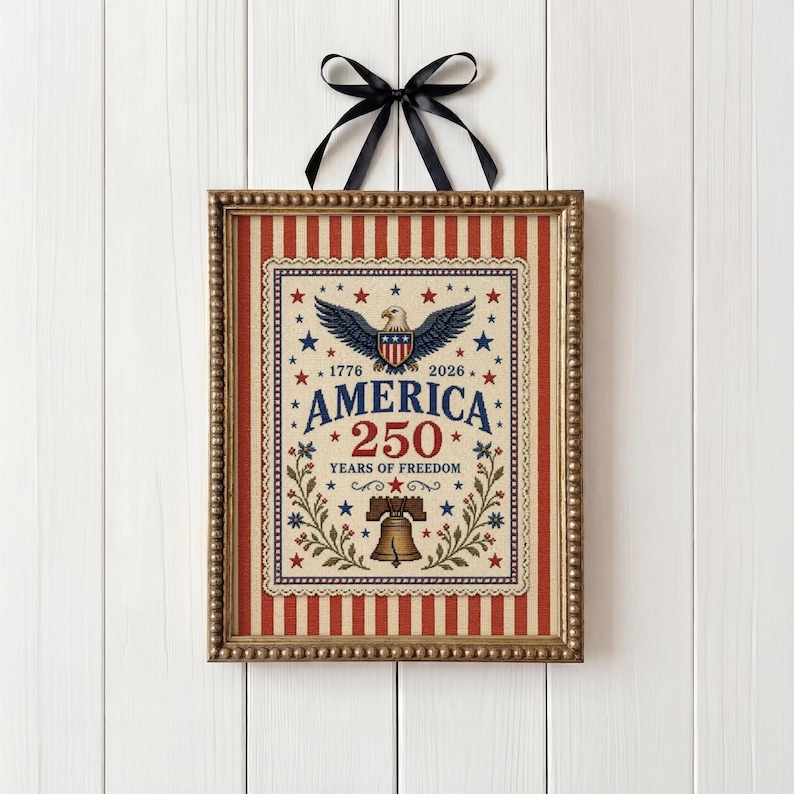 Puede incluir: Obra de arte patri&oacute;tica enmarcada con una combinaci&oacute;n de colores rojo, blanco y azul. El dise&ntilde;o presenta un &aacute;guila, estrellas y el texto "AMERICA 250 YEARS OF FREEDOM" dentro de un borde decorativo. Una cinta negra est&aacute; adjunta para colgar.
