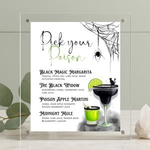 May include: A Halloween-themed cocktail menu displayed in a clear acrylic frame. The menu features a spider web and spider graphic, with cocktail names like "Black Magic Margarita" and "The Black Widow". The drinks are illustrated with lime slices and a black cat.