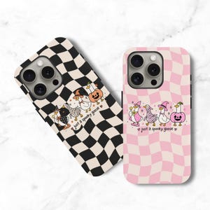 Peut inclure: Deux coques de téléphone avec un motif damier ondulé et des illustrations d'oies en costumes d'Halloween. L'une est noire et blanche, l'autre rose et blanche. Les deux portent l'inscription "just a spooky goose" accompagnée de petites étoiles.