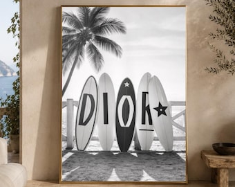 May include: A black and white wall art print featuring five surfboards standing in a row on a sandy beach. Each surfboard displays a single letter or symbol, collectively spelling DIOR with a star icon on the final board, set against a palm tree.