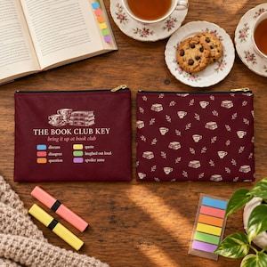 May include: Two rectangular zippered pouches in deep burgundy. One features a graphic of stacked books and teacups with the text THE BOOK CLUB KEY, bring it up at book club, and a color-coded legend. The other has a repeating pattern of books and teacups.