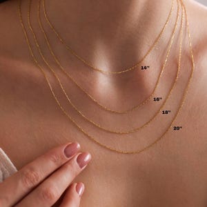 May include: Four gold chains of different lengths, 14 inches, 16 inches, 18 inches, and 20 inches, are shown on a model's neck.