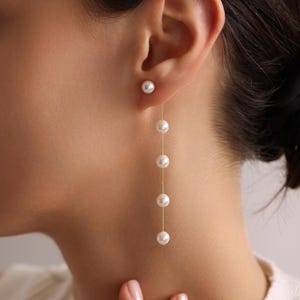 May include: A pair of gold earrings with a single pearl stud and a dangling chain of pearls.
