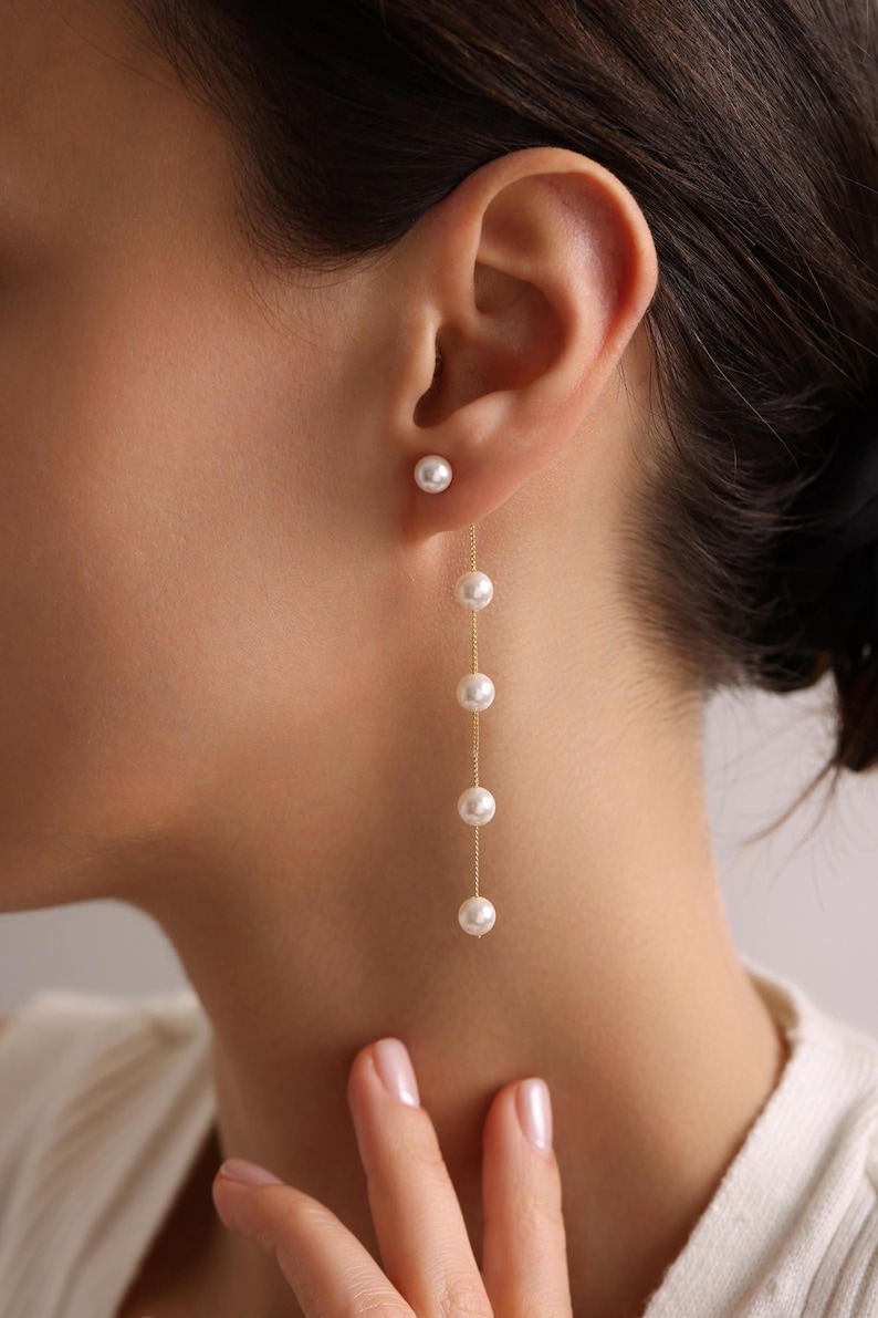 May include: A pair of gold earrings with a single pearl stud and a dangling chain of pearls.
