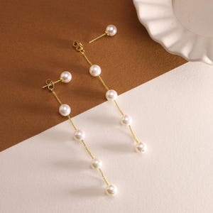 May include: A pair of gold pearl drop earrings with a single pearl stud earring. The drop earrings have five pearls on each chain.