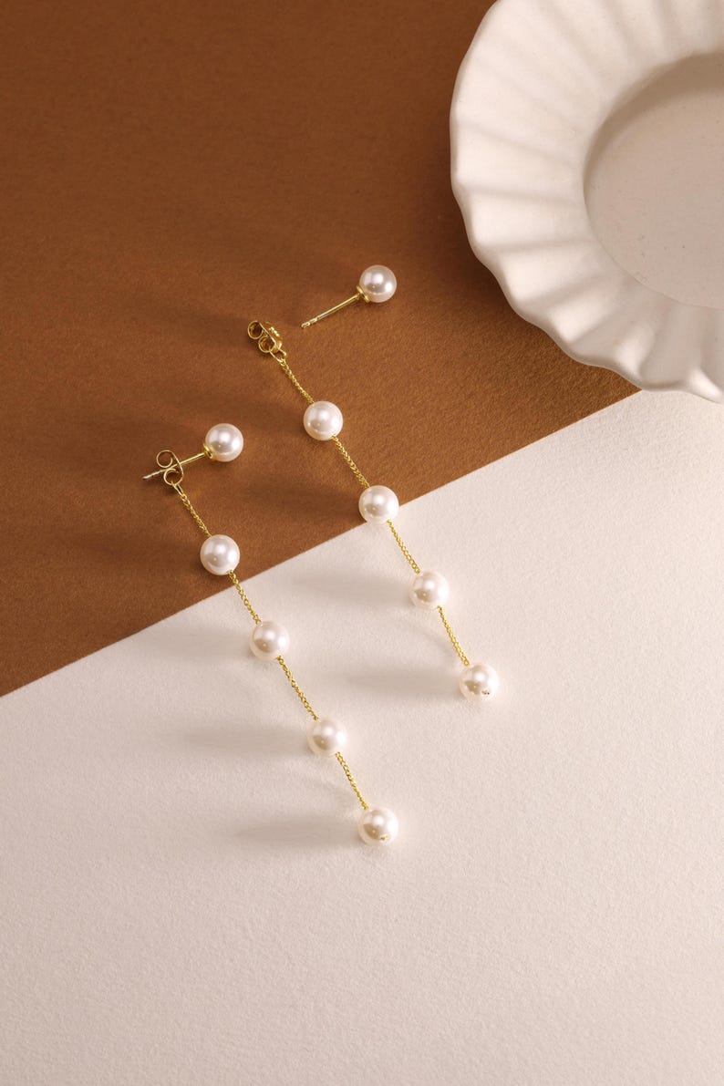 May include: A pair of gold pearl drop earrings with a single pearl stud earring. The drop earrings have five pearls on each chain.
