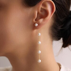 May include: A pair of gold earrings with a single pearl at the top and a chain of pearls dangling down.