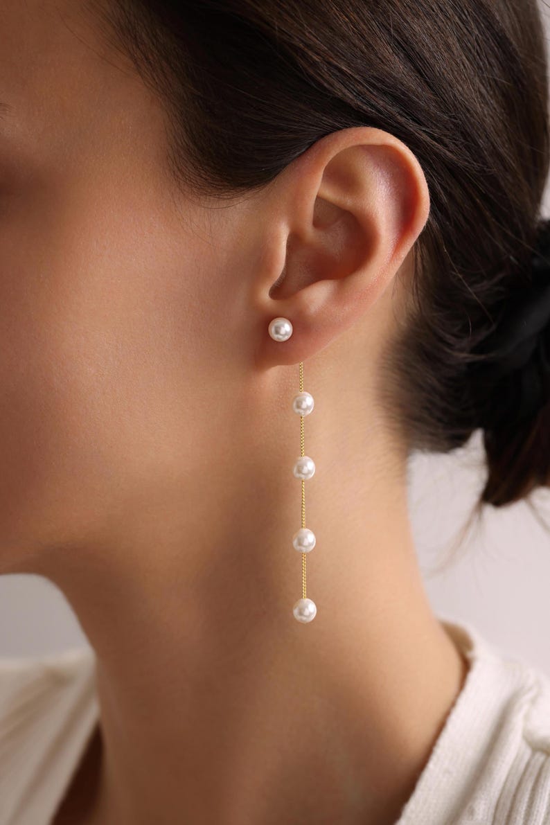 May include: A pair of gold earrings with a single pearl at the top and a chain of pearls dangling down.