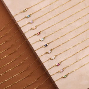 May include: A set of gold necklaces with colorful gemstone accents. Each necklace features a delicate chain with two small, rectangular gemstones.