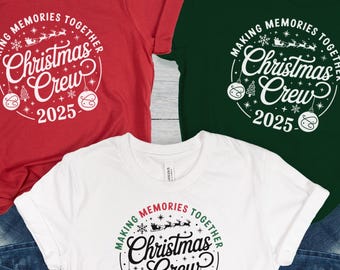 May include: Three t-shirts in red, white, and green, each featuring a circular design with the text "Making Memories Together Christmas Crew 2025". The shirts are paired with blue denim jeans, suggesting a holiday theme.
