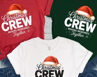 May include: Three short-sleeved t-shirts in red, white, and green, each featuring a Santa hat graphic and the text "Christmas CREW MAKING MEMORIES Together". The shirts are paired with blue denim jeans.
