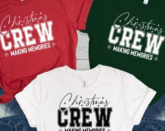 May include: Three short-sleeved t-shirts in red, white, and green, each with the text "Christmas CREW MAKING MEMORIES" in a collegiate style. The shirts are paired with blue denim jeans, suggesting a casual holiday theme.