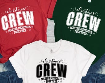May include: Three short-sleeved t-shirts in red, white, and green, each with the text "Christmas CREW" in a bold font. Below the word "CREW" is the phrase "MAKING MEMORIES TOGETHER" in a smaller font. The shirts are paired with blue jeans.