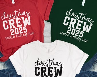 May include: Three t-shirts in red, white, and green, each with the text "Christmas CREW 2025 FORCED FAMILY FUN" in a festive font. The shirts are paired with blue denim jeans, suggesting a holiday theme.