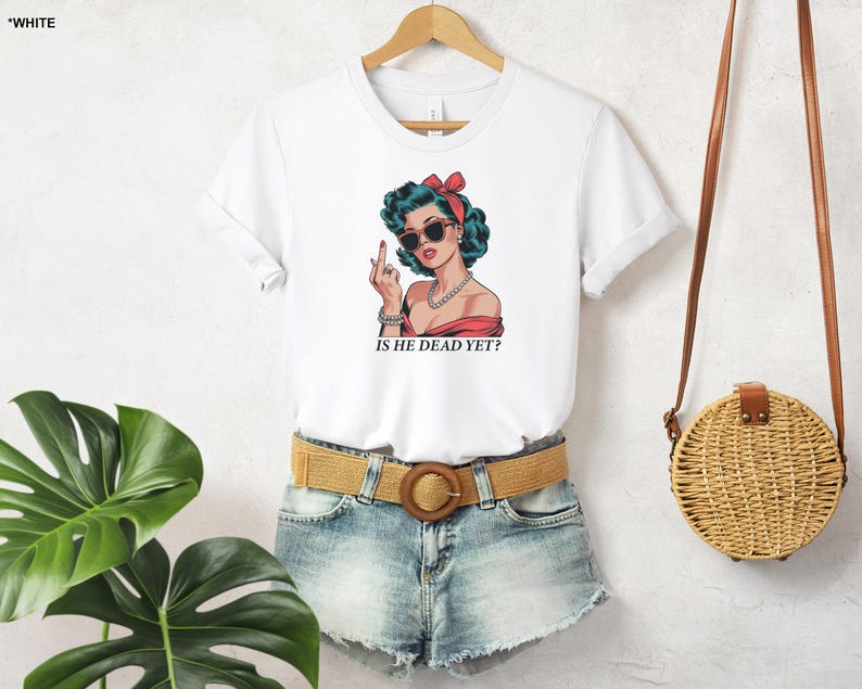 May include: White t-shirt with a cartoon image of a woman wearing sunglasses and a red headband. The text "Is he dead yet?" is printed below the image.