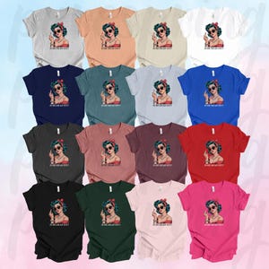May include: A collection of 12 t-shirts in various colors featuring a retro-style illustration of a woman with blue hair and red lipstick. The woman is giving a middle finger and the text "Is he dead yet?" is printed on the shirt.