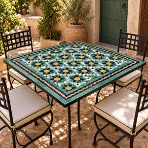 Peut inclure: Une table carrée d'extérieur avec un plateau en mosaïque présentant un motif géométrique d'étoiles répétitif dans des tons de vert, jaune et blanc, entourée de quatre chaises en métal noir avec des coussins blanc cassé et un passepoil vert.
