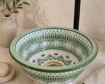 May include: A round ceramic vessel sink featuring intricate green and white geometric patterns and floral motifs. The basin has a wide rim and a central brass-toned drain. A tall, matte black faucet is positioned behind the sink basin.