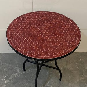 Könnte beinhalten: Ein runder Beistelltisch mit einer Mosaik-Tischplatte in Rot- und Brauntönen. Die Tischplatte wird von einem schwarzen Metallrahmen und Beinen getragen. Der Tisch hat einen Durchmesser von ca. 61 cm.