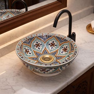 Könnte beinhalten: Ein dekoratives Keramikwaschbecken mit einem Blumenmuster in Blau, Braun und Weiß. Es ist auf einer Marmorarbeitsplatte mit einem schwarzen Wasserhahn installiert. Ein goldener Seifenspender und ein Tablett mit gerollten weißen Handtüchern sind ebenfalls zu sehen.