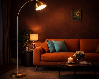 May include: A tall, arched floor lamp with a brushed gold finish and a dome-shaped shade. The lamp features a slender metal stem and a circular base, emitting a warm, downward-facing light that illuminates the surrounding living room space.