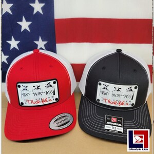 May include: Two trucker hats with a white mesh back and a black and white cow graphic with the text "EAT MOR ASS" and "Thick-fil-a" on the front. The hats are red and black.