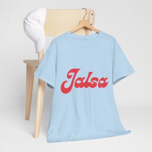 Puede incluir: Una camiseta azul claro con un gráfico rojo de estilo retro que dice "Jalsa" en la parte delantera.