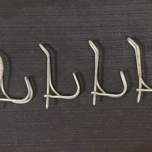May include: Four silver-toned metal wall hooks, each featuring a double-pronged design with a threaded screw base for mounting. The hooks have a curved shape and show slight signs of oxidation or rust on the metal surfaces of the prongs.