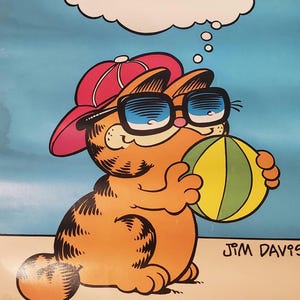 Puede incluir: Un póster vintage que muestra a un gato atigrado naranja con una gorra de béisbol roja y gafas de sol negras, sosteniendo una pelota de playa amarilla y verde. Una burbuja de pensamiento contiene el texto i live for saturdays! y Jim Davis.
