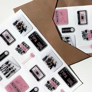 May include: A collection of stickers featuring the text "BLACKPINK" and images of a music cassette, a license plate that says "TYPA GIRL", and a group of people. The stickers are in pink, black, and white.