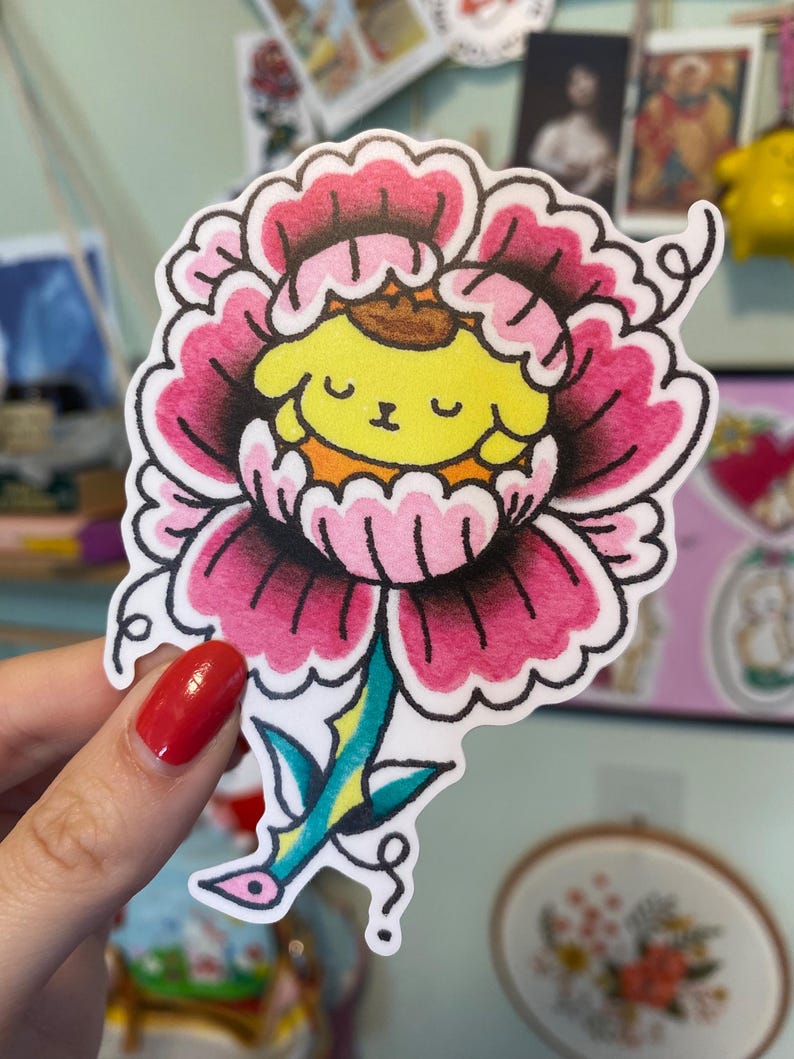May include: A colorful sticker featuring a cartoon character inside a pink and black flower. The character has yellow fur, a brown hat, and a smiling face. The flower has a green and blue stem.