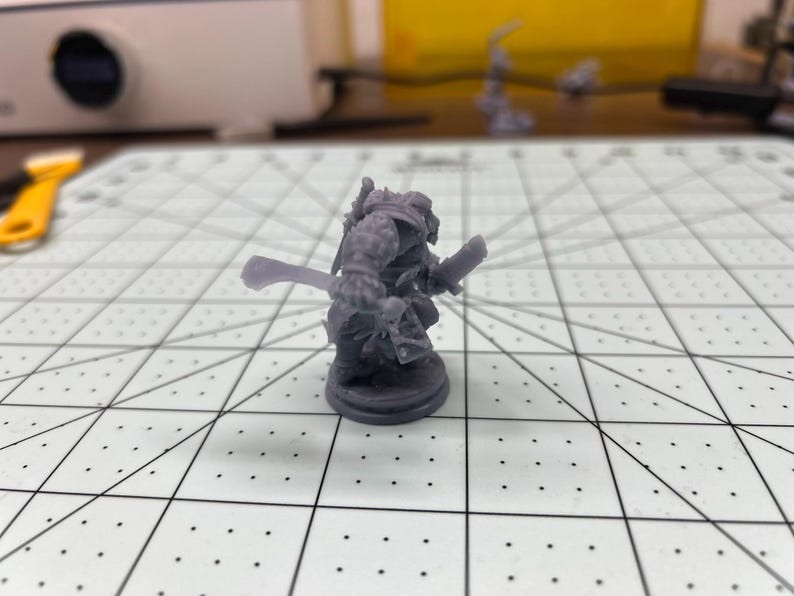 May include: A gray plastic miniature figurine of a warrior holding a sword and shield. The figurine is standing on a round base.