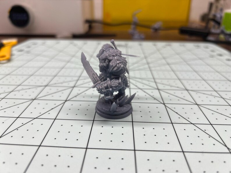 May include: A gray plastic miniature figurine of a fantasy character holding a sword. The figurine is standing on a round base.