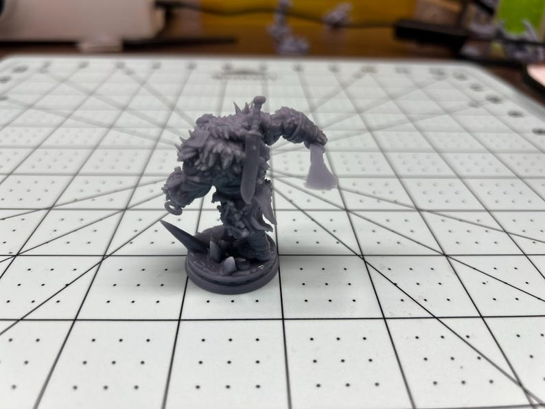 May include: A gray 3D printed miniature of a furry, humanoid creature holding an axe. The miniature is standing on a round base.
