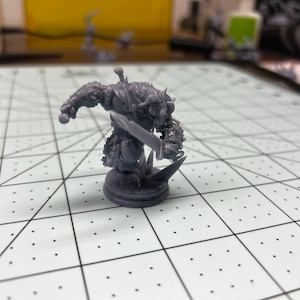 May include: A gray plastic miniature figurine of a fantasy creature holding a sword. The figurine is standing on a round base.