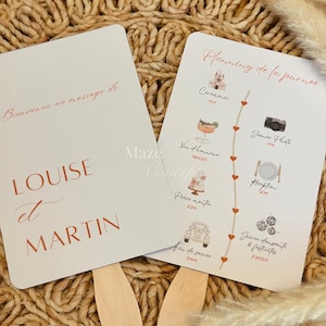 Peut inclure: Deux cartons éventails de mariage blancs avec des manches en bois. L'un des cartons indique "Louise et Martin" en texte couleur cuivre. L'autre présente un calendrier de mariage avec des illustrations et du texte en cuivre.